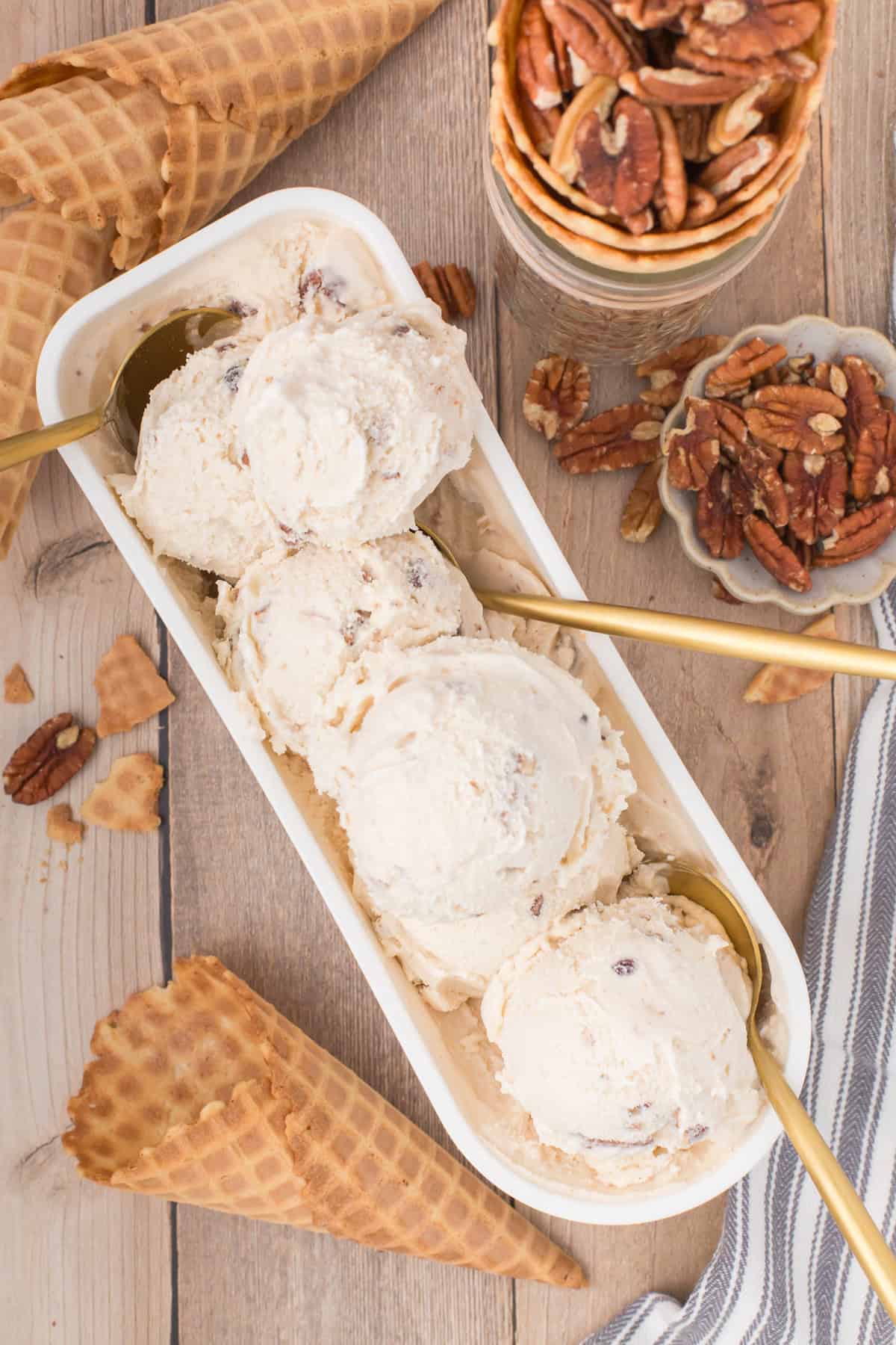 overhead shot showing butter pecan ice cream scoops rolled up inside of a white rectangular ice cream tub