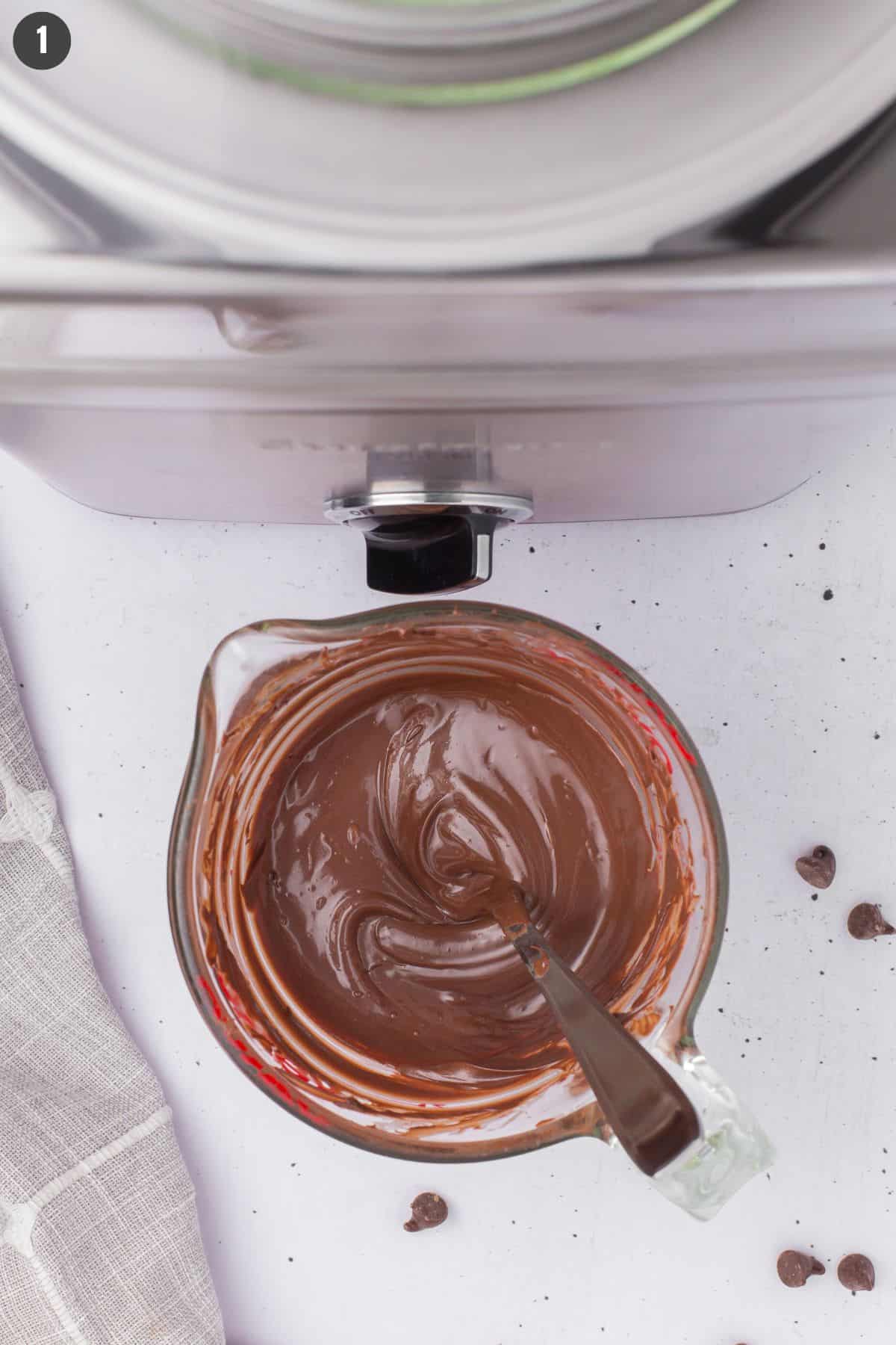 overhead shot showing melted chocolate chips in a small glass measuring cup with a freezer bowl ice cream maker in the background