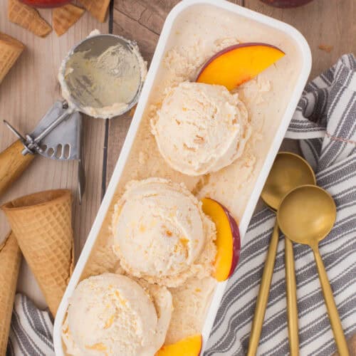 peach cobbler ice cream in an ice cream tub with fresh peach slices on top