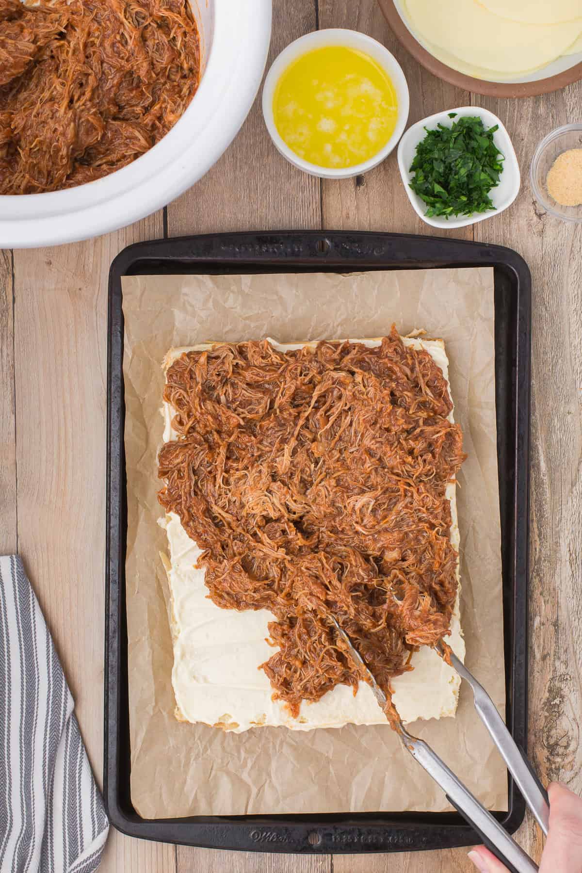 using tongs to pile bbq chicken on Hawaiian rolls