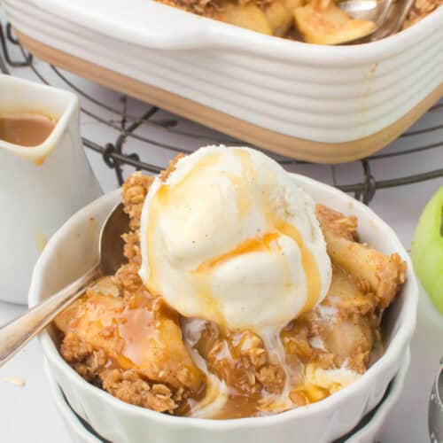 old-fashioned apple crisp in a small white ramekin dish with caramel sauce and a scoop of vanilla ice cream on top