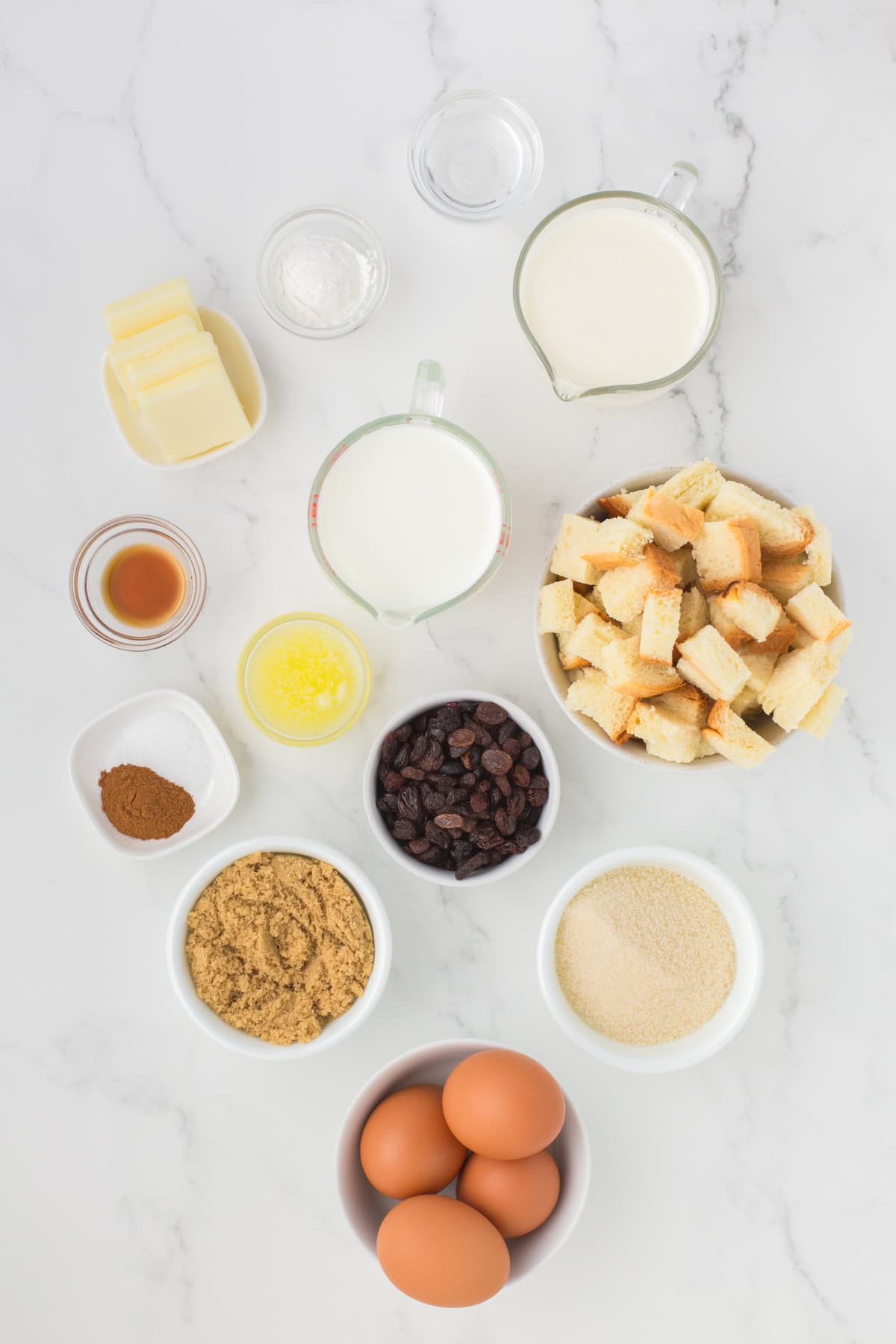 old fashioned bread pudding with vanilla sauce ingredients lined out on a white countertop