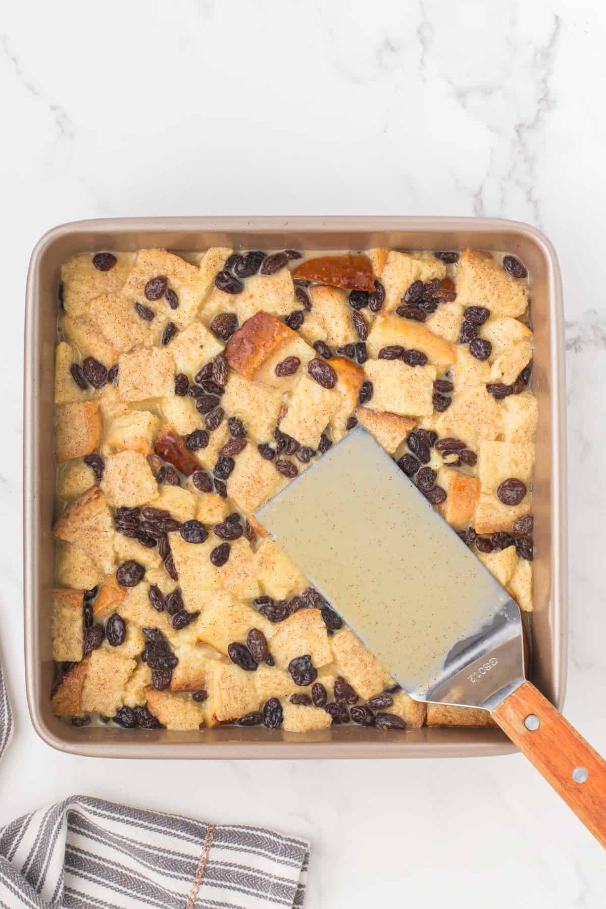 freshly baked bread pudding with raisins in a 9x9 casserole dish with a metal spatula resting on top