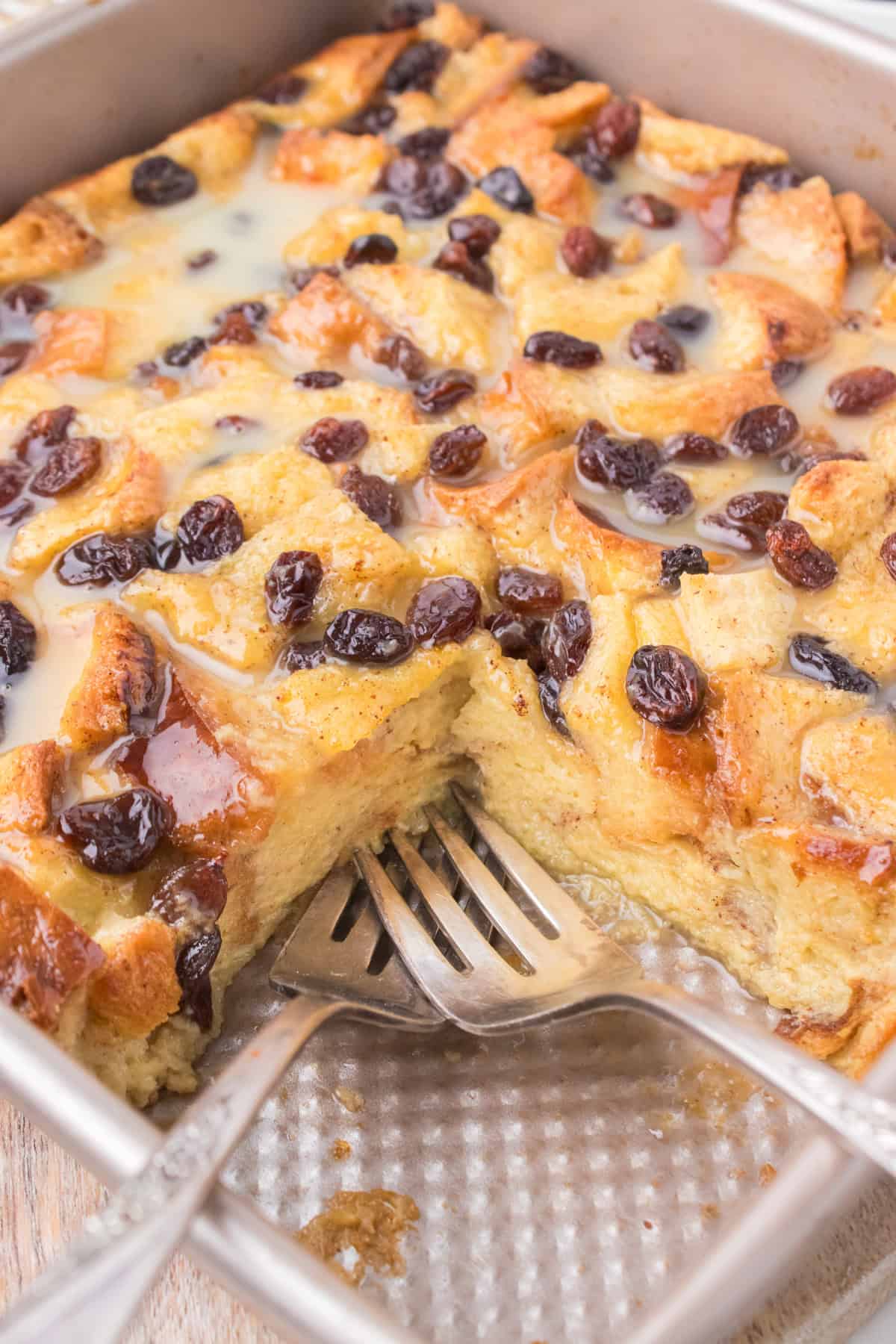 old fashioned bread pudding with vanilla sauce in a gray 9x9 pan with 2 forks