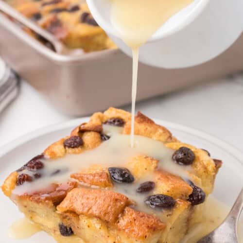 old fashioned bread pudding on a small white saucer with warm vanilla sauce being drizzled over top out of a white pitcher