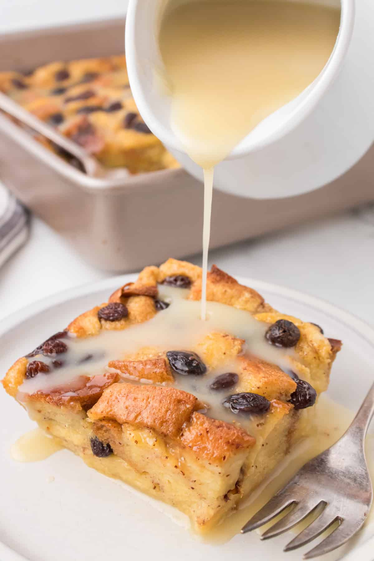 old fashioned bread pudding on a small white saucer with warm vanilla sauce being drizzled over top out of a white pitcher
