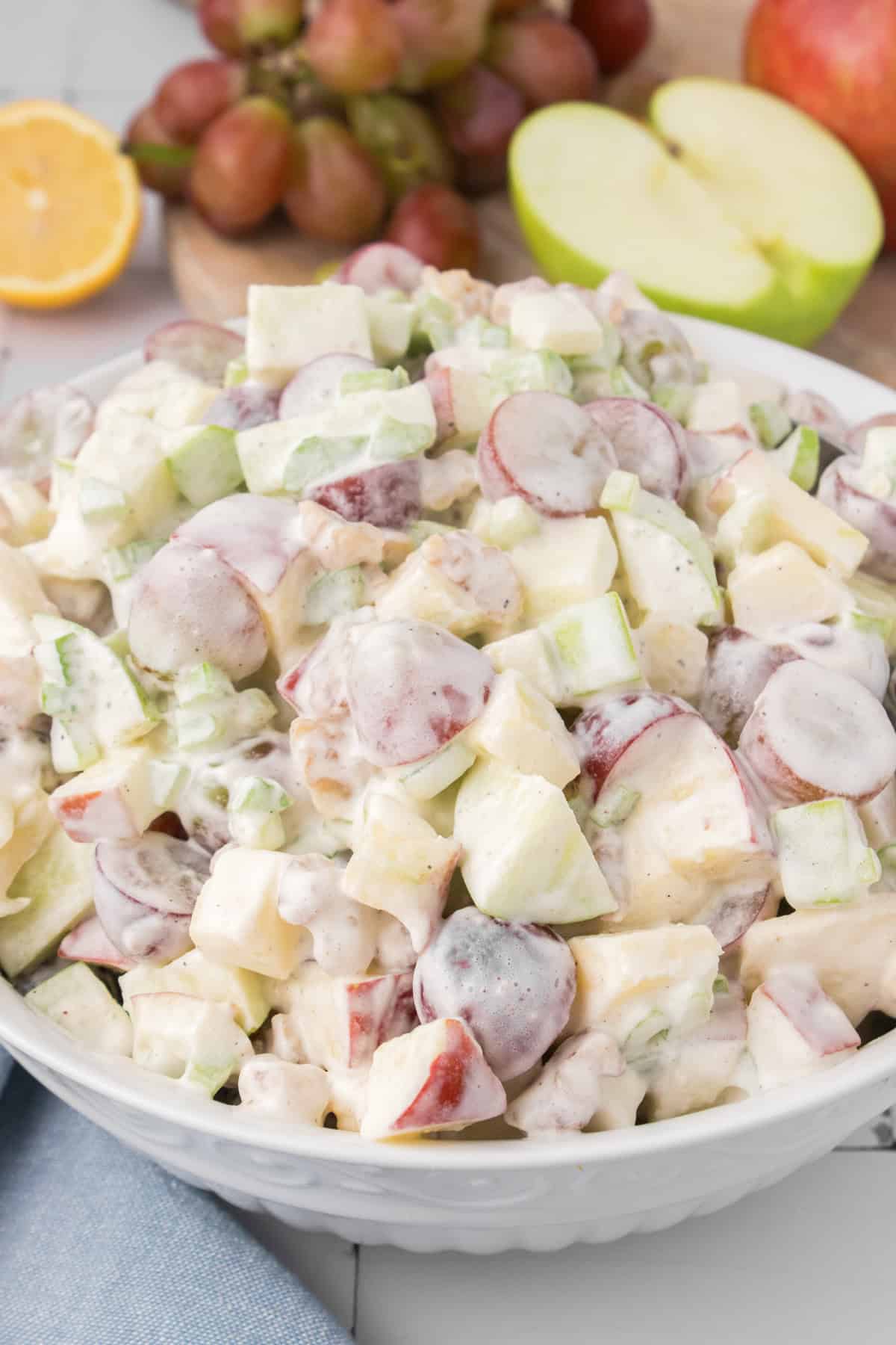 easy Waldorf salad ready to serve in a white mixing bowl with fresh fruit in the background